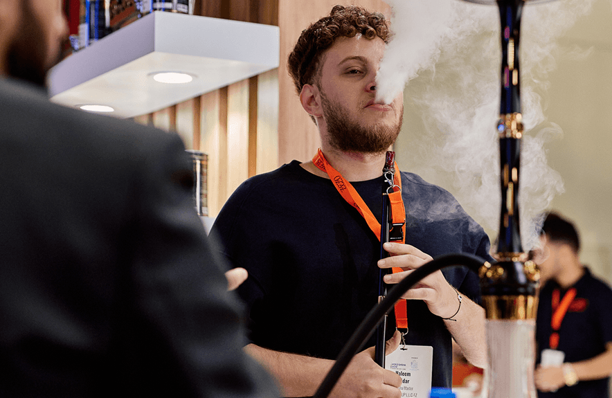 A guest exhaling smoke beside a gold-stemmed hookah at a ZEZO event