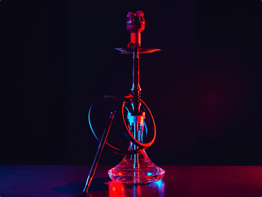 A glass-base hookah lit by red and blue studio lighting, hose coiled at its base